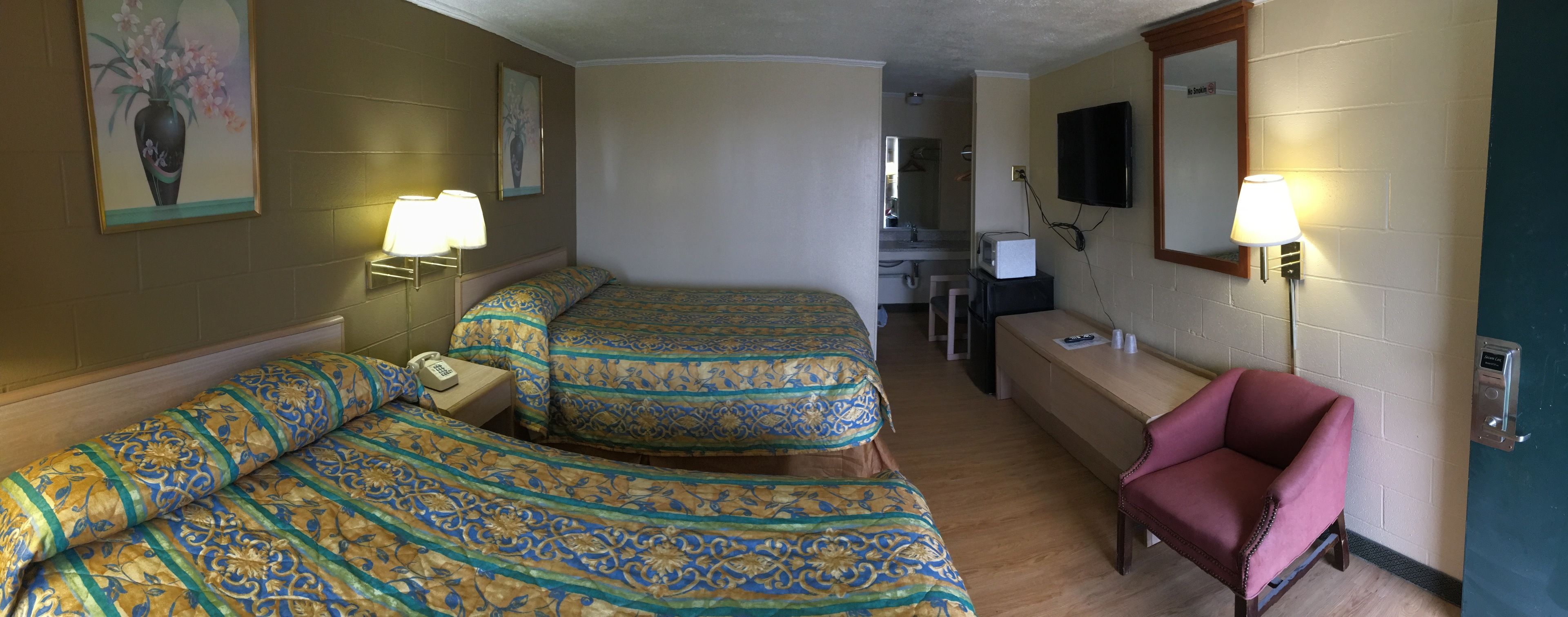 A hotel room with two beds, a desk, a chair, and a TV.