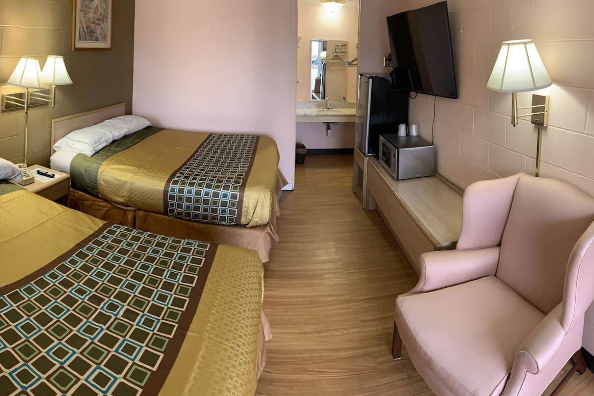 A hotel room with two beds, a chair, a TV, and a small kitchenette.