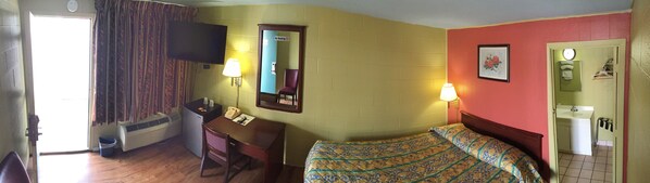 A hotel room with a bed, a desk with a telephone, a chair, a television, and a mirror.