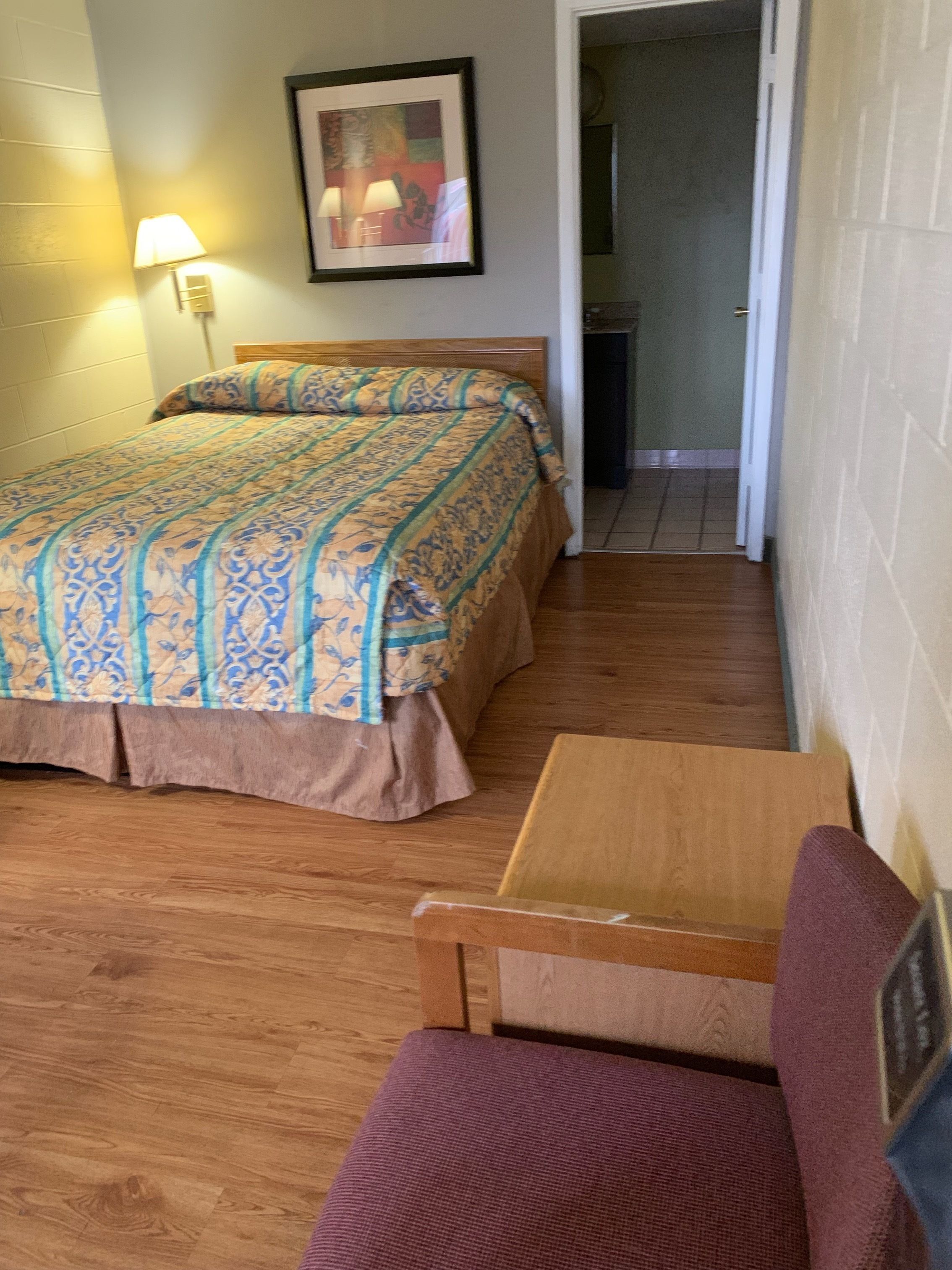 Een slaapkamer met een bed, een stoel, een tafel, een lamp en een schilderij aan de muur.
