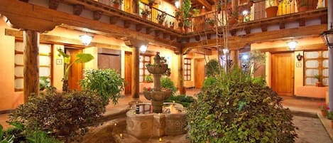 Un patio con una fuente, plantas en macetas y balcones de madera.