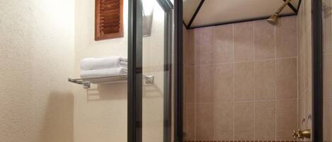 A bathroom with a glass-enclosed shower, a toilet, and a shelf with towels.