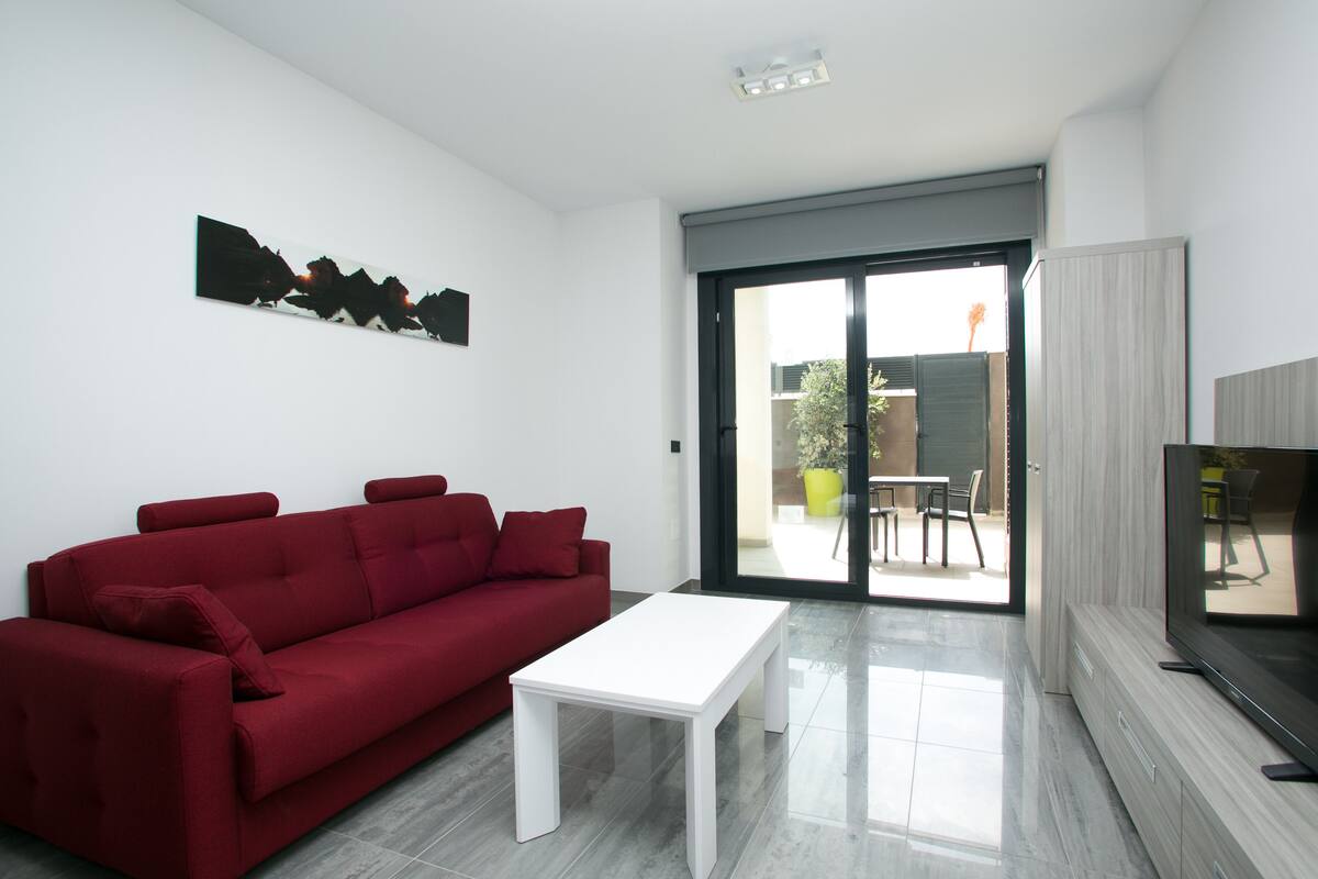 Un salon moderne avec un canapé rouge, une table basse blanche et un téléviseur à écran plat.