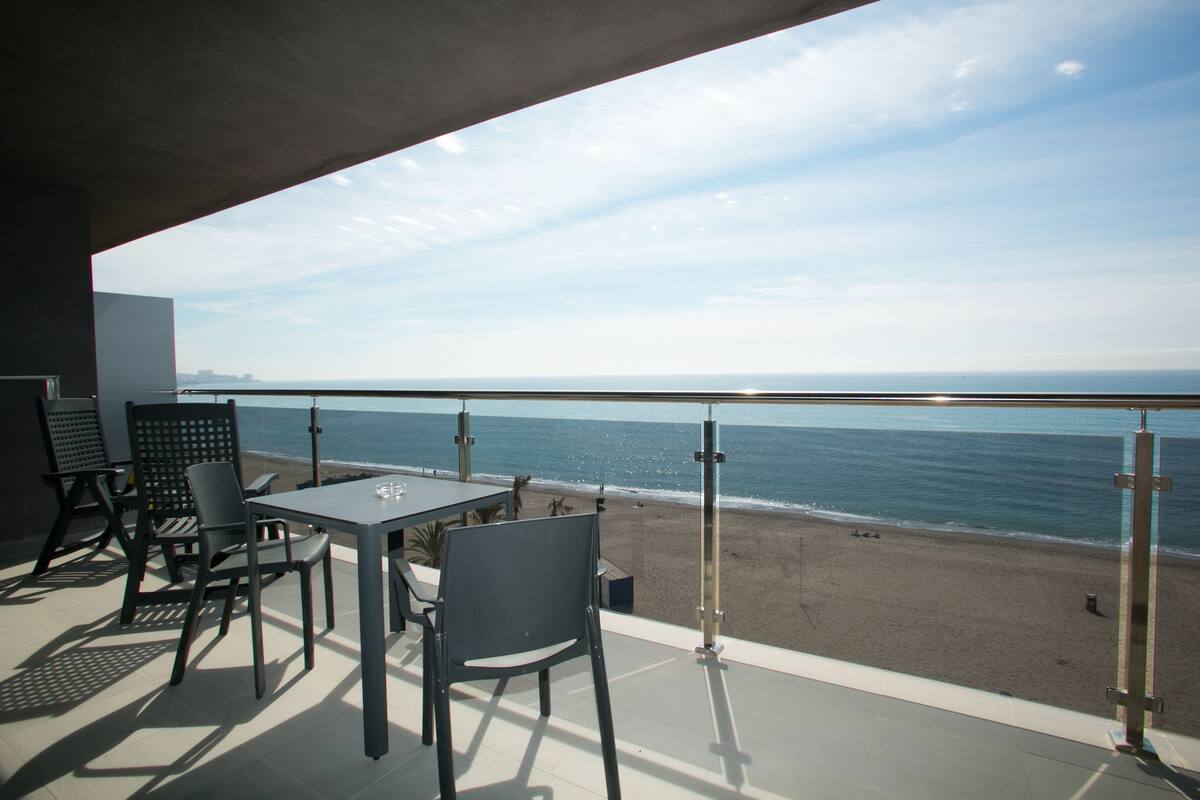 Un balcon avec une table et des chaises, donnant sur une plage et l’océan.