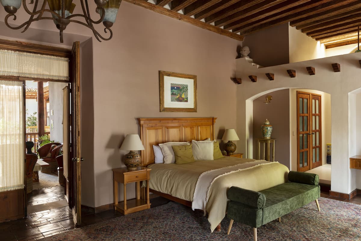 A bedroom with a wooden headboard, a bed with a green upholstered bench, two bedside tables with lamps, and a framed picture on the wall.