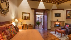A cozy bedroom with a large bed, a wooden desk, a chair, a fireplace, and a television. - Hotel Casa del Naranjo (Patzcuaro)