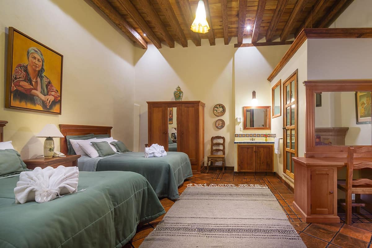 A hotel room with two beds, wooden furniture, a mirror, and artwork on the walls.