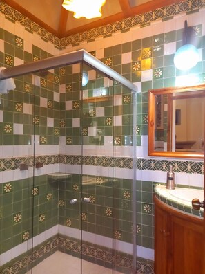 A bathroom with green and white checkered tiles, a glass shower enclosure, and a wooden vanity with a sink. - Hotel Casa del Naranjo (Patzcuaro)