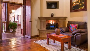 A cozy living room with a fireplace, a leather sofa, and a television mounted on the wall. - Hotel Casa del Naranjo (Patzcuaro)
