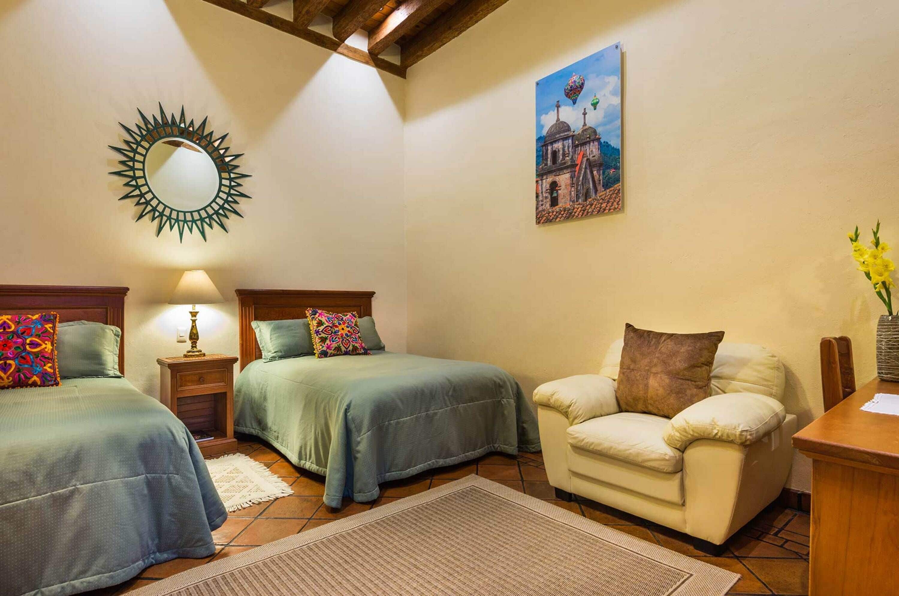 Un dormitorio con dos camas, una silla, un escritorio, un espejo y un cuadro en la pared.