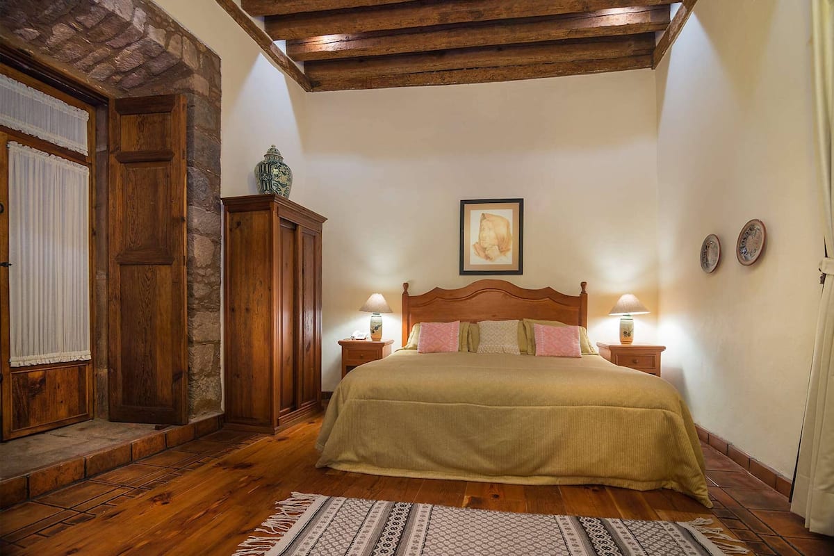 A bedroom with a wooden bed, two bedside tables with lamps, a stone wall, and a framed picture on the wall.