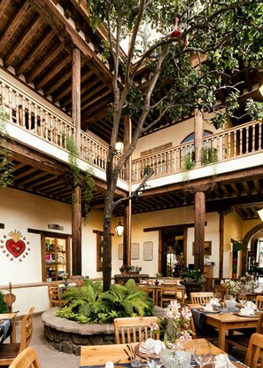 A traditional inn with a rustic wooden interior, featuring a central courtyard with tables and chairs, surrounded by balconies and a large tree. - Hotel Casa del Naranjo (Patzcuaro)