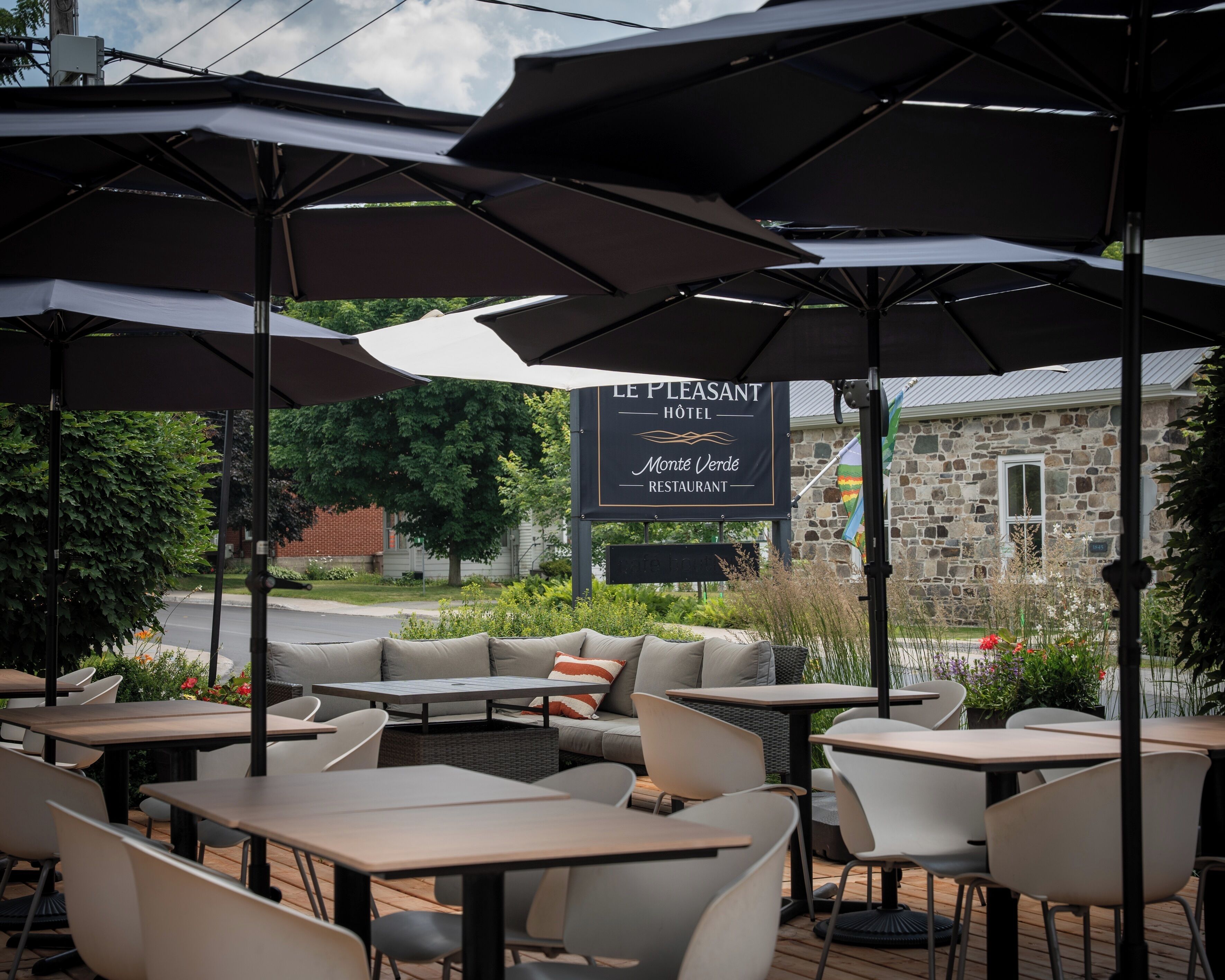 Outdoor seating with umbrellas, a sign for Le Plaisant Hotel, and a stone building in the background.