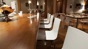 Una larga mesa de comedor con sillas blancas, una barra de madera y luminarias colgantes.