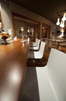 Une longue table à manger avec des chaises blanches, un comptoir de bar en bois et des luminaires suspendus.
