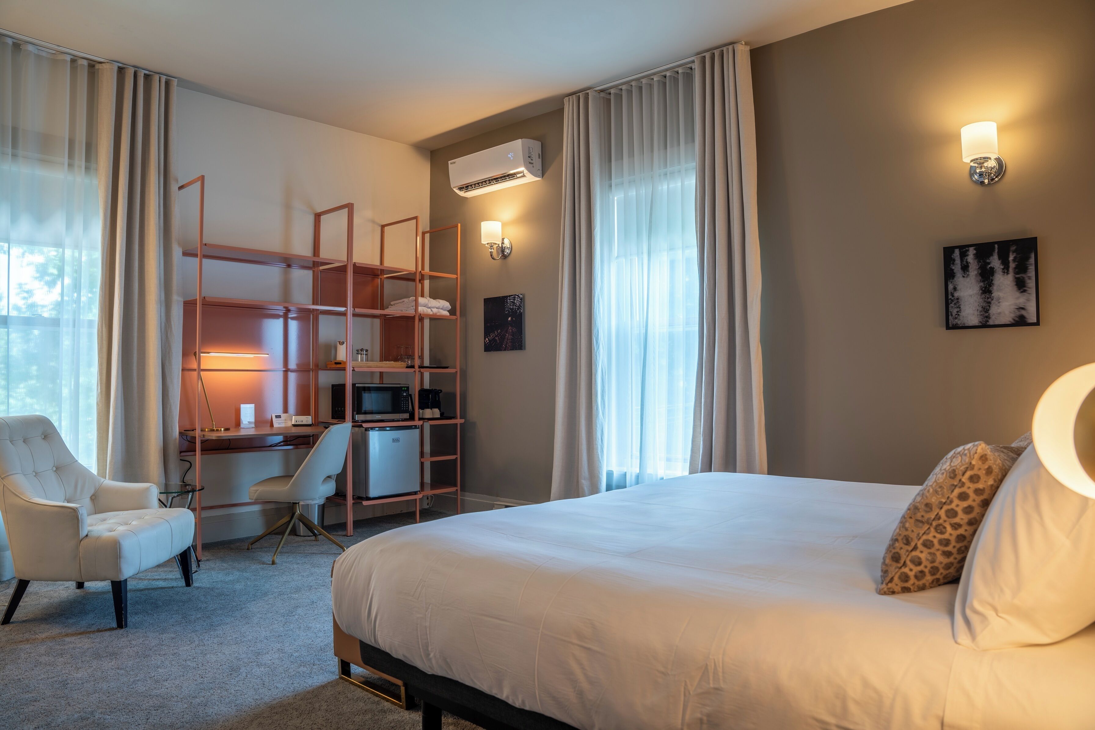 Habitación de hotel con cama, escritorio con computadora, silla, armario y aire acondicionado instalado en la pared.