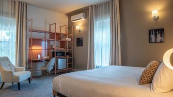 Habitación de hotel con cama, escritorio con computadora, silla, armario y aire acondicionado instalado en la pared.