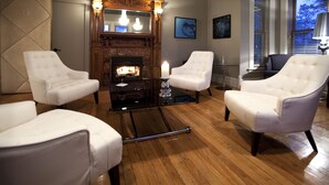 Una habitación con chimenea, sillones blancos y suelo de madera.