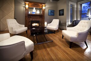 Une pièce avec une cheminée, des fauteuils blancs et un plancher en bois.