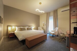Une chambre d’hôtel avec un grand lit, un coin salon avec un banc, un bureau et une chaise.