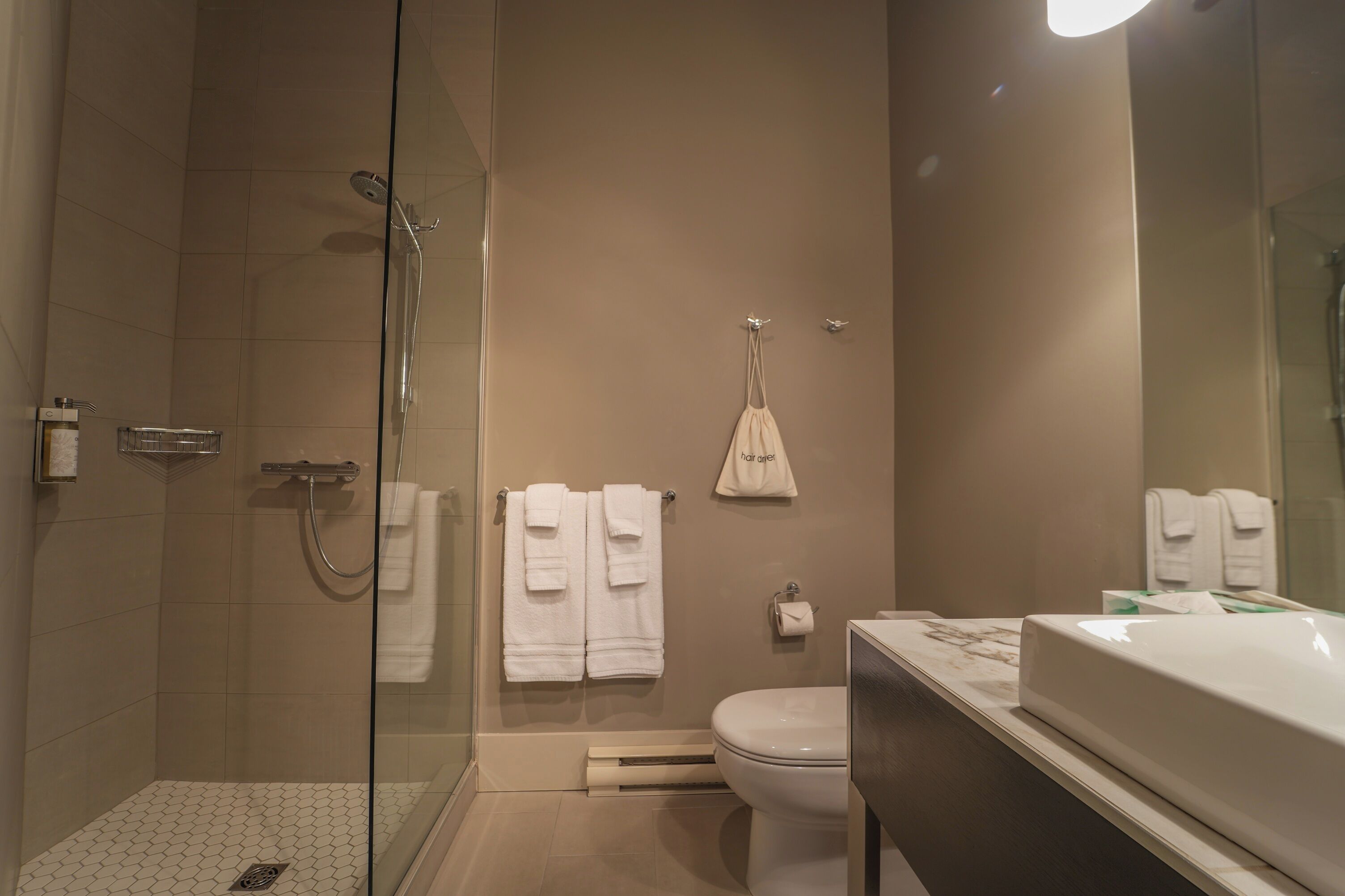Un baño moderno con ducha envuelta en cristal, inodoro y lavamanos con espejo.