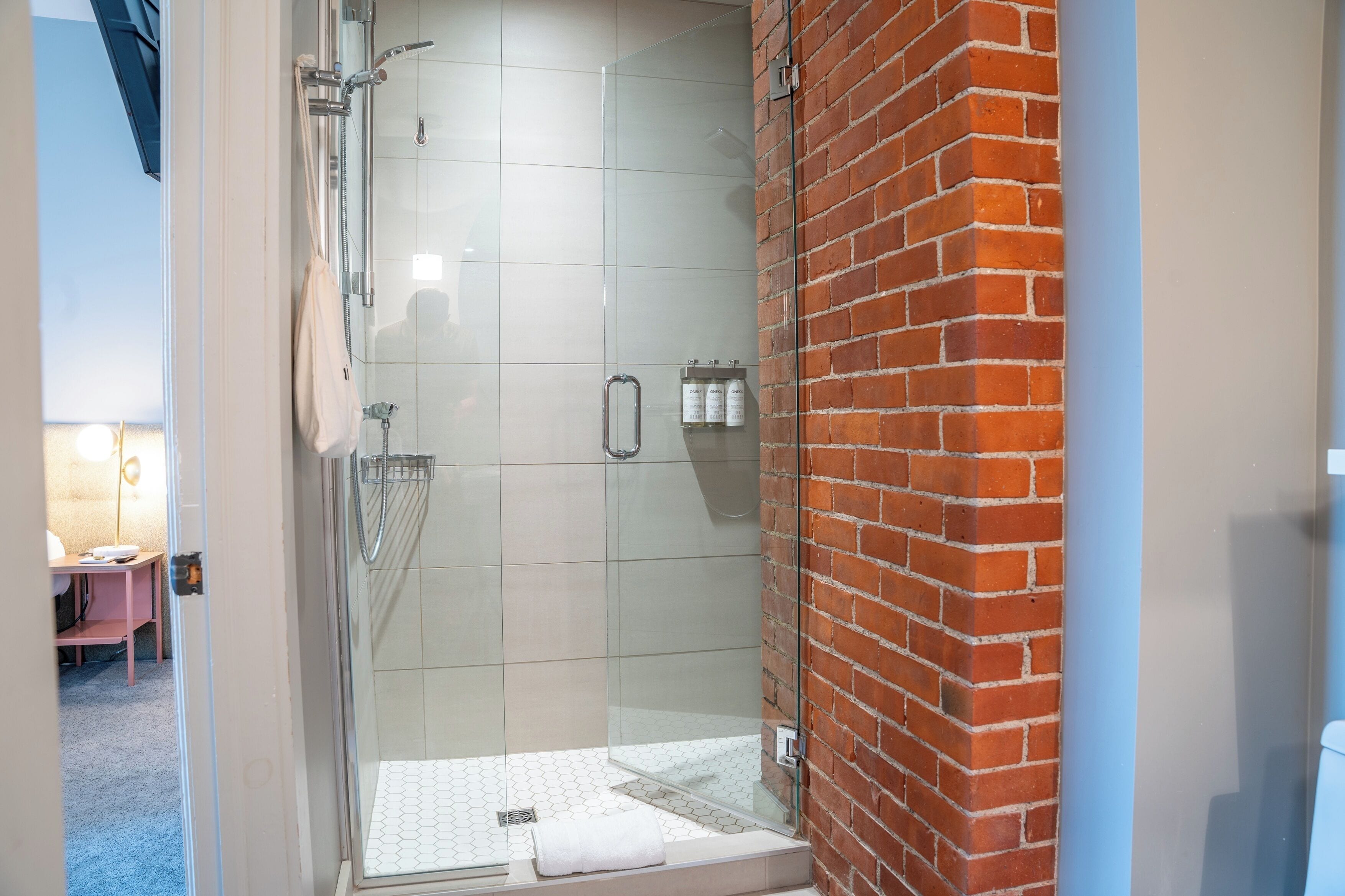A glass-enclosed shower with a tiled floor, a towel rack, and a brick wall.