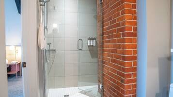 A glass-enclosed shower with a tiled floor, a towel rack, and a brick wall.