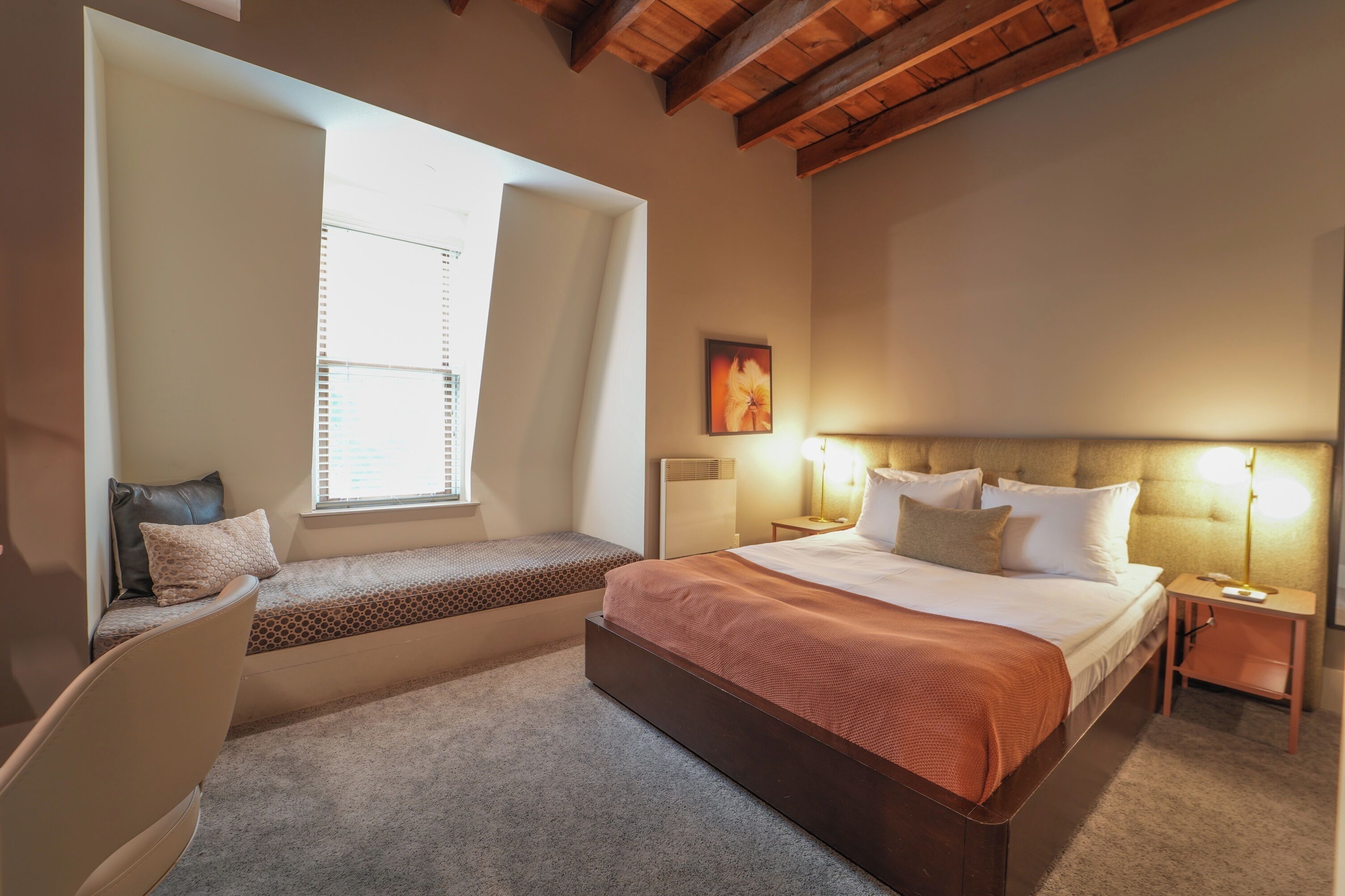 Une chambre à coucher avec un grand lit, un banc, une table de chevet et une fenêtre.