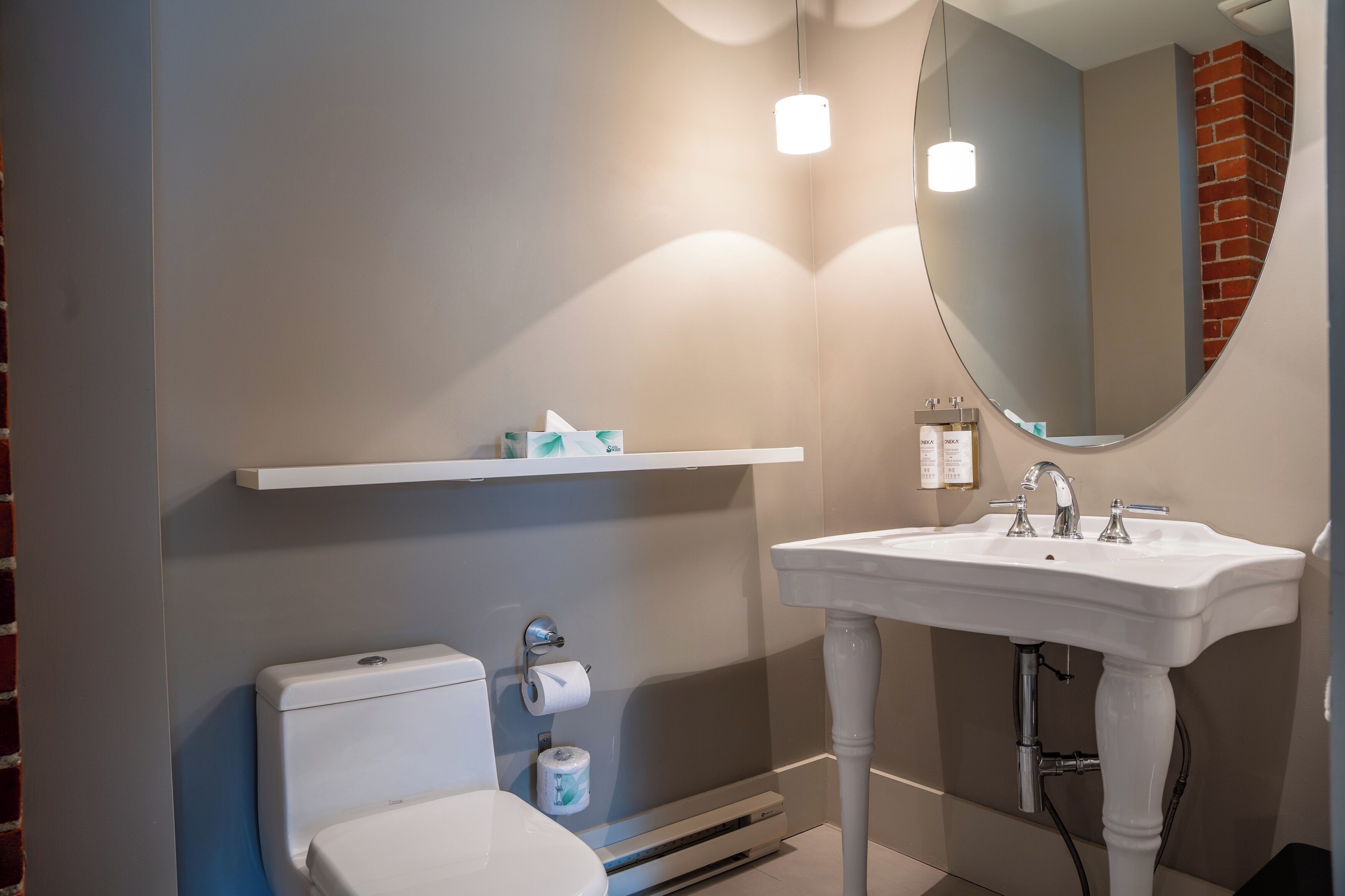 A bathroom with a toilet, a sink, a mirror, and a shelf with toiletries.