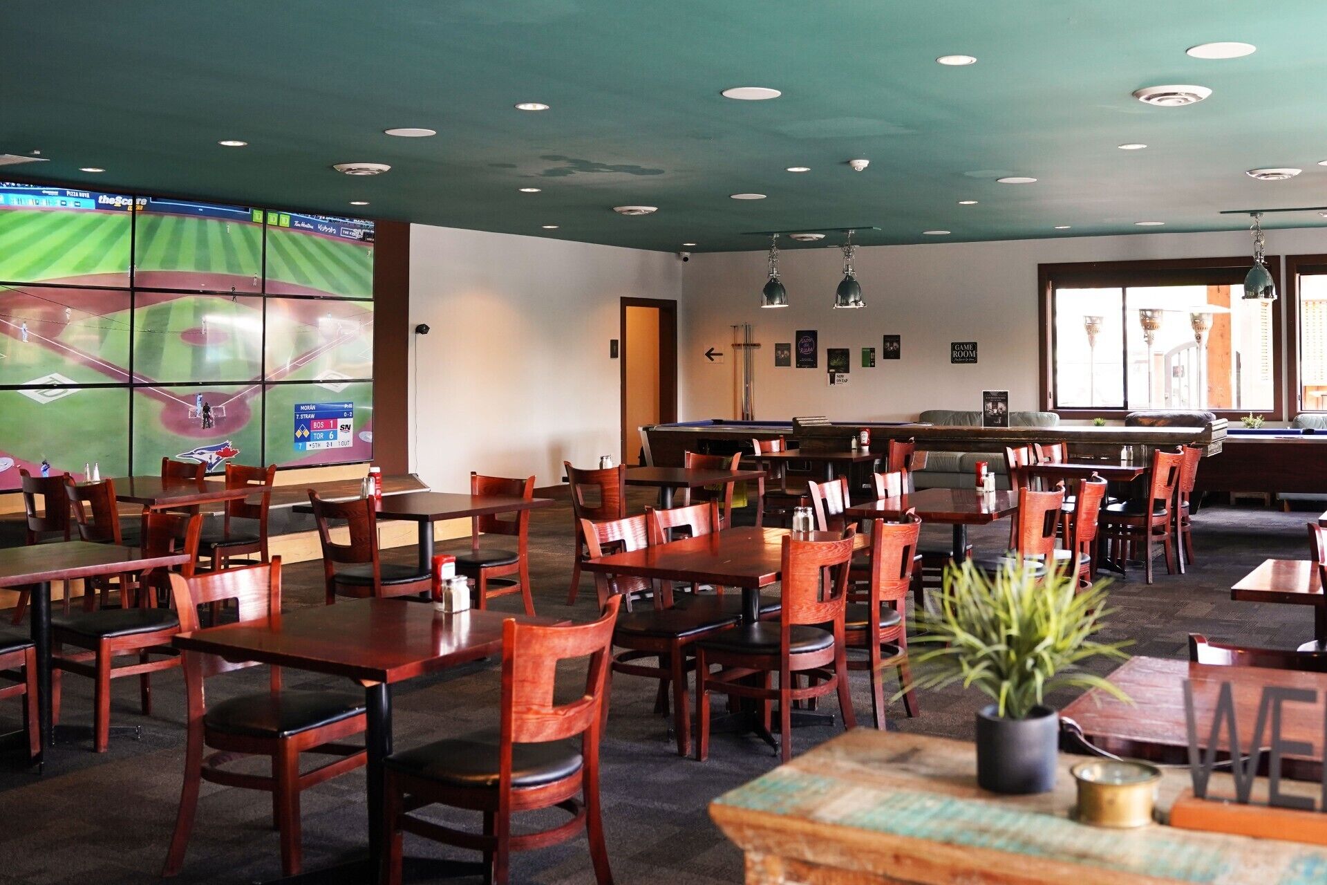 A restaurant with multiple tables and chairs, a pool table, and a large screen displaying a sports game.