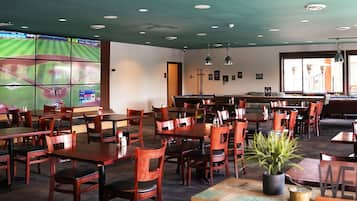 A restaurant with multiple tables and chairs, a pool table, and a large screen displaying a sports game.