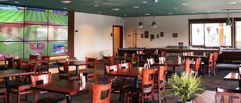 A restaurant with multiple tables and chairs, a pool table, and a large screen displaying a sports game.