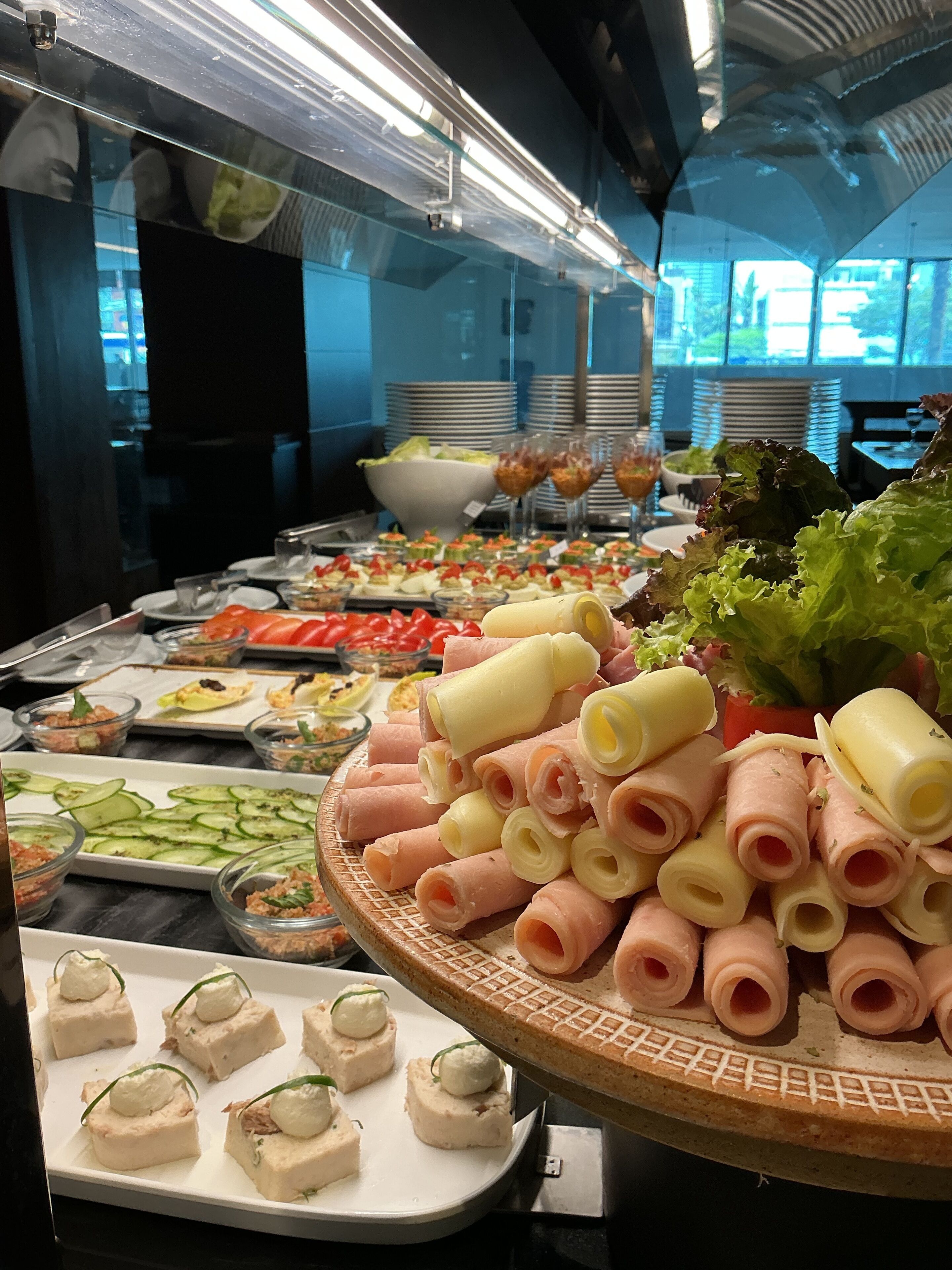 Un bufé con diversos alimentos, entre ellos, carnes enrolladas, queso y verduras.