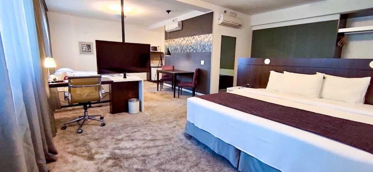 Habitación de hotel con una cama grande, un escritorio con silla, un televisor y un pequeño rincón de descanso.