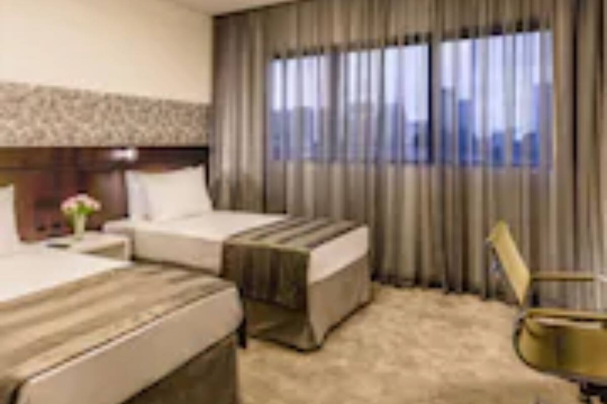 A hotel room with two beds, a desk, a chair, and a large window with curtains.