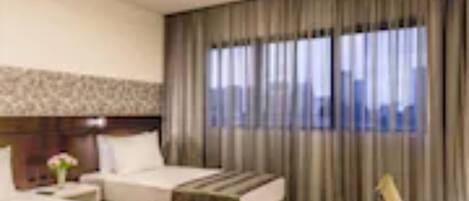 Habitación de hotel con dos camas, un escritorio, una silla y un ventanal con cortinas.