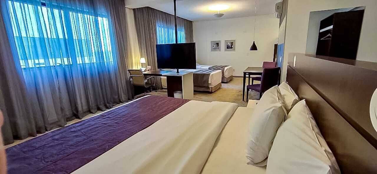 A hotel room with a large bed, a desk with a computer, a TV, and a seating area with a couch and chairs.