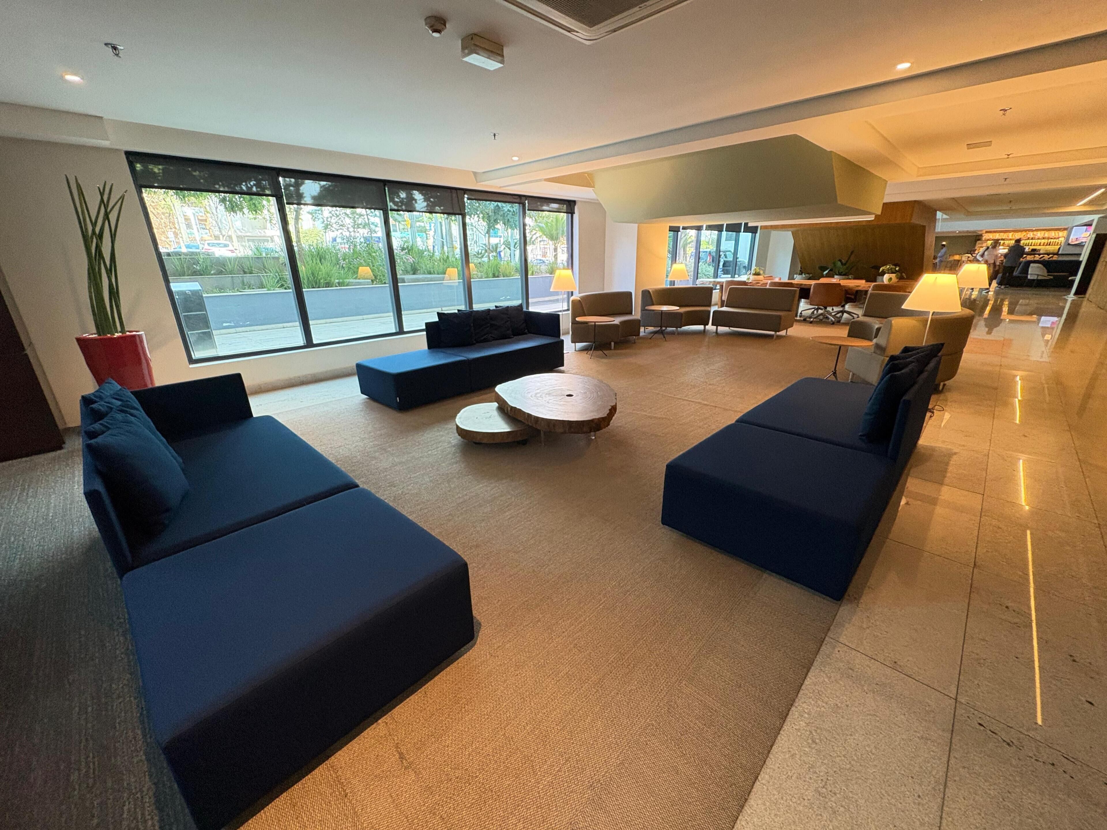 A spacious lobby with dark blue sofas, a round coffee table, and large windows offering a view of the outdoors.