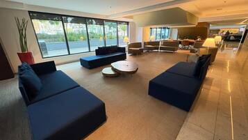 A spacious lobby with dark blue sofas, a round coffee table, and large windows offering a view of the outdoors.