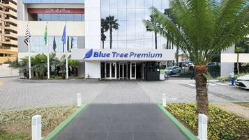 Der Eingang zum Blue Tree Premium mit einem gepflasterten Weg, der zum Eingang führt, umgeben von Palmen und einem modernen Gebäude im Hintergrund.