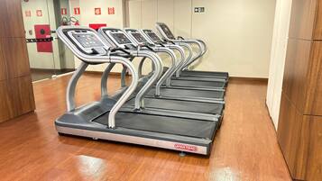 Una fila di tapis roulant in palestra, con pavimento in legno e uno specchio a parete.