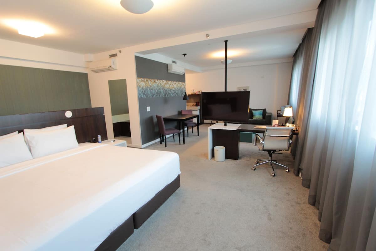 A hotel room with a large bed, a desk with a chair, a television, and a lamp.