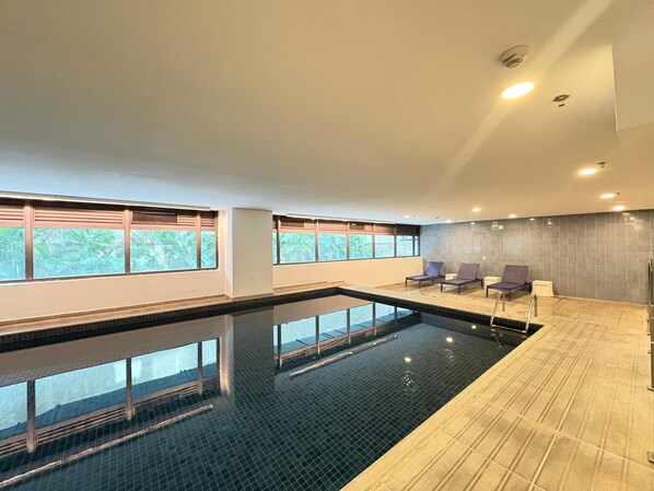 Une piscine intérieure avec des parois en verre transparent, un sol carrelé et quelques chaises longues.