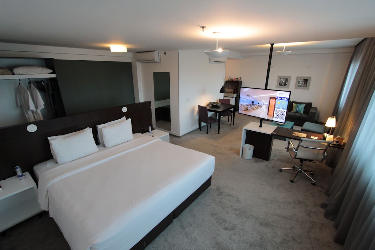 A hotel room with a large bed, a desk with a chair, a television, and a small table.
