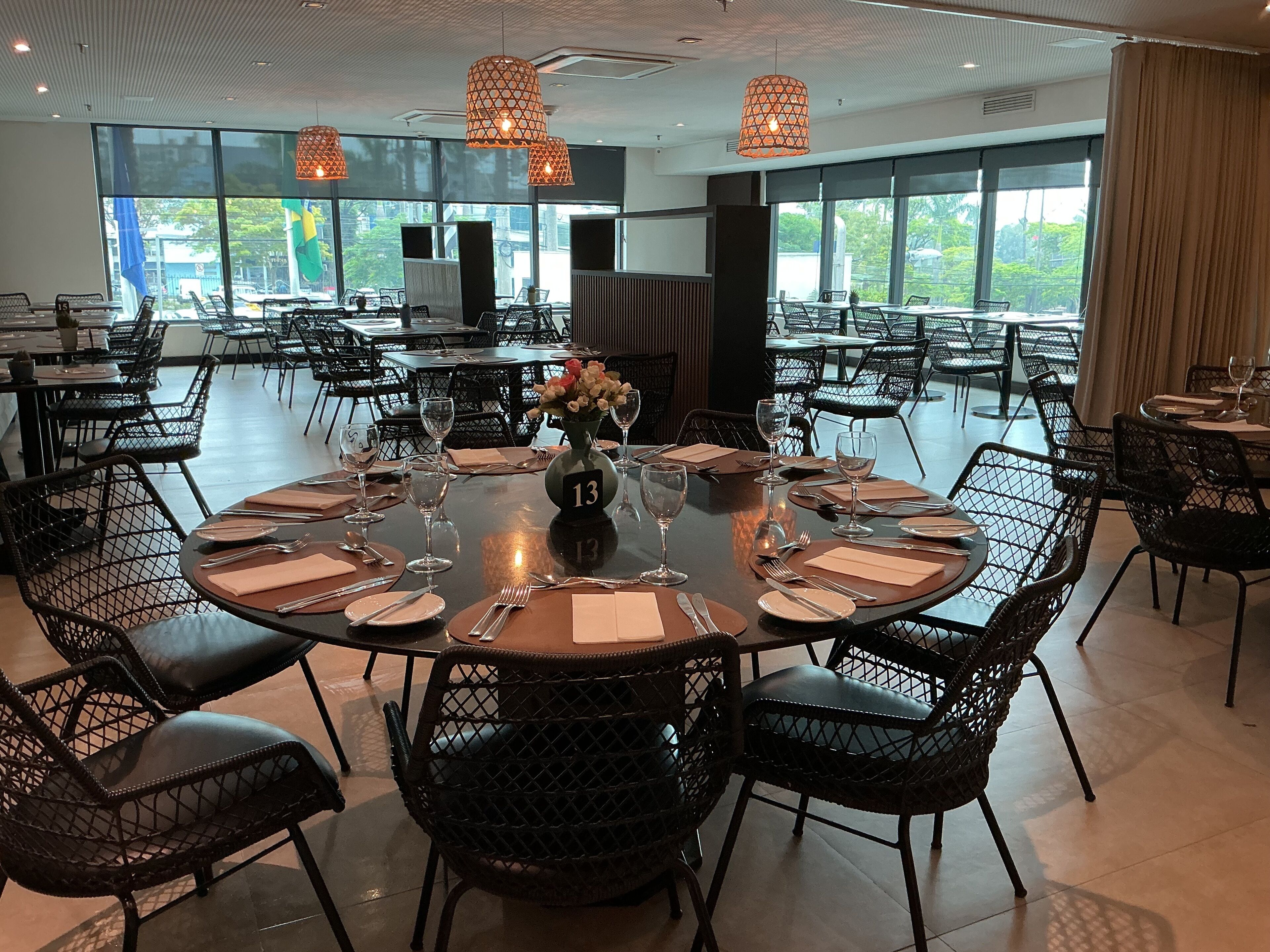A spacious dining area with round tables, black mesh chairs, and pendant lighting.