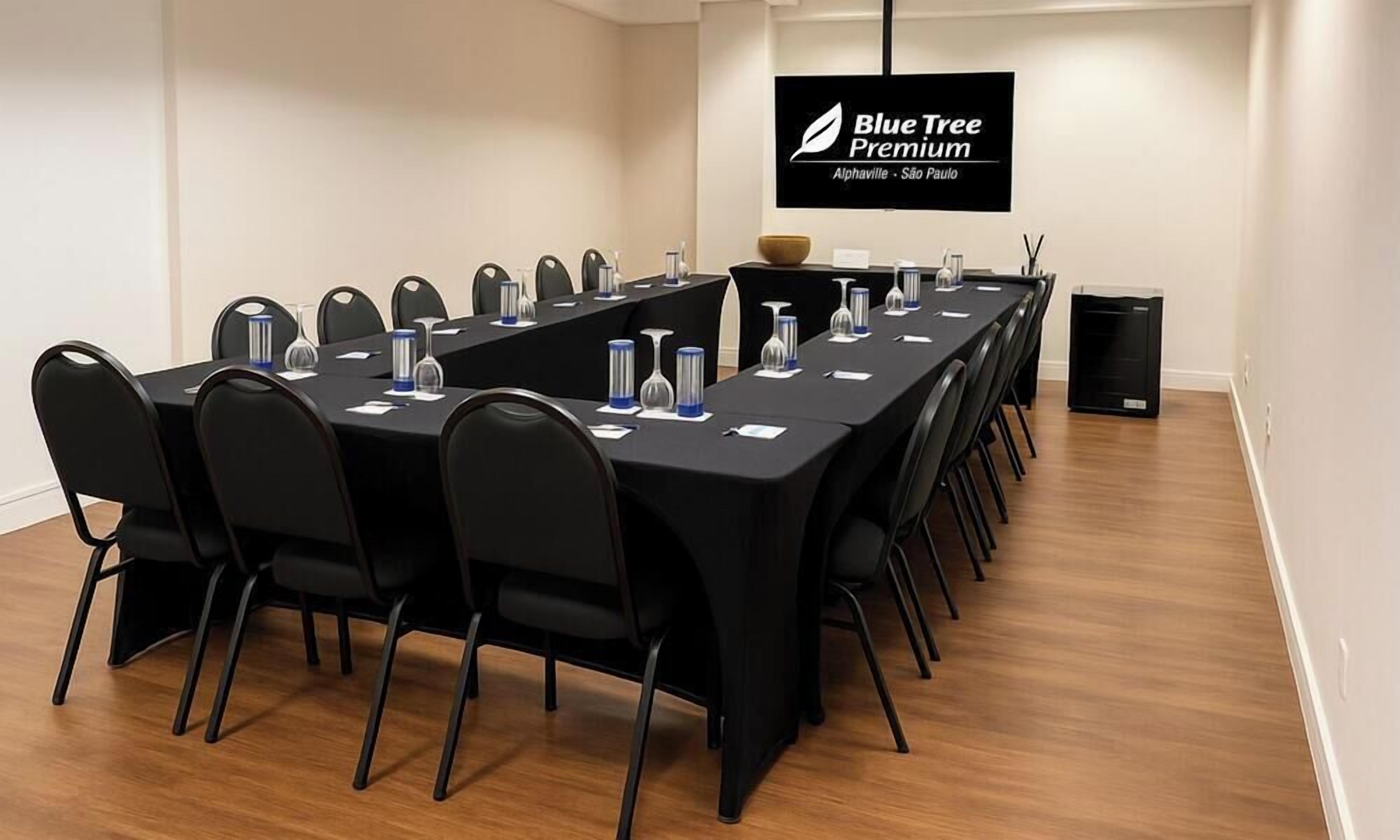 Ein Konferenzraum mit einem langen Tisch, schwarzen Stühlen und einem Flachbildfernseher, der "Blue Tree Premium" anzeigt.