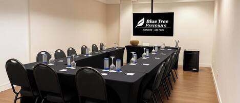 Ein Konferenzraum mit einem langen Tisch, schwarzen Stühlen und einem Flachbildfernseher, der "Blue Tree Premium" anzeigt.