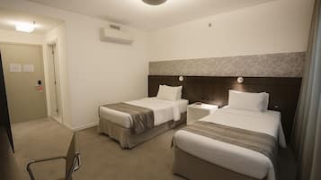 A hotel room with two beds, a bedside table, an air conditioning unit, a door, and a chair.