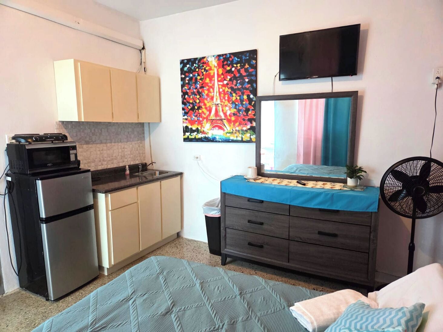 A compact living space with a kitchenette, a bed, a TV, and a fan.