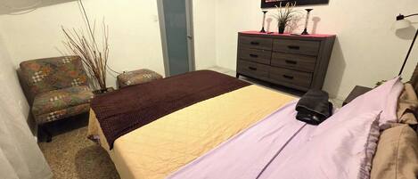 A bedroom with a bed, a chair, a dresser, a TV, and a door.